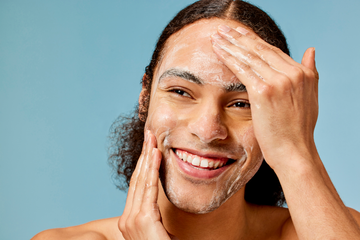 Man Close-up using Acure cleanser on his face on a light blue background